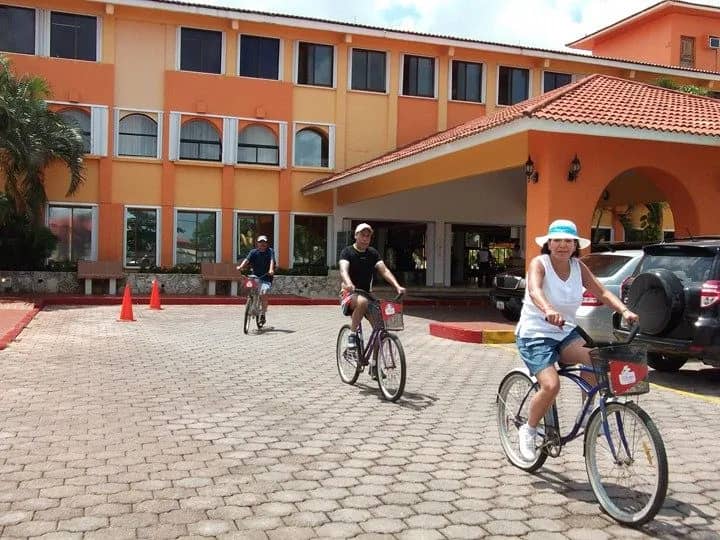 People riding bikes in front of a hotel. Enjoying a sunny day, they pedal along the street, creating a lively atmosphere. People riding bikes in front of a hotel. Enjoying a sunny day, they pedal along the street, creating a lively atmosphere.